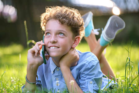 Happy young teenage boy talking on mobile phone outdoors in summer park. Online friendship conceptの写真素材