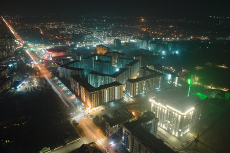 Aerial view of high rise apartment buildings and bright illuminated streets in city residential area at night. Dark urban landscapeの写真素材