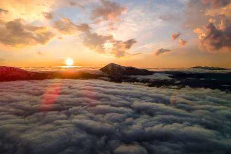 Aerial view of vibrant sunrise over white dense clouds with distant dark mountains on horizon