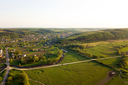 Aerial landscape view of green cultivated agricultural fields with growing crops and distant village...