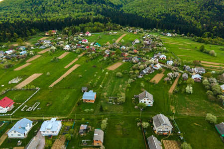 Aerial landscape view of village houses and distant green cultivated agricultural fields with growing crops on bright summer dayの写真素材