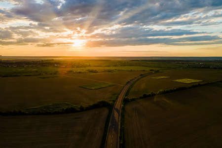 Aerial view of intercity road with fast driving cars between farmland fields at sunset. Top view from drone of highway traffic in eveningの写真素材