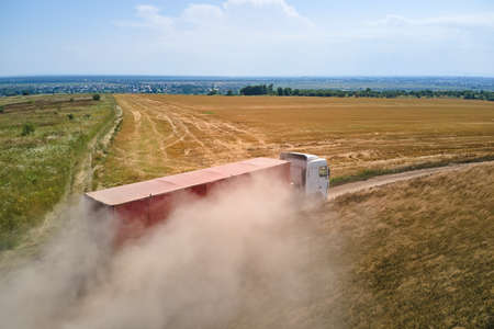 Aerial view of lorry cargo truck driving on dirt road between agricultural wheat fields. Transportation of grain after being harvested by combine harvester during harvesting seasonの写真素材