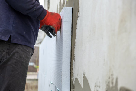 Construction worker installing polystyrene insulation sheets on house facade wall for thermal...