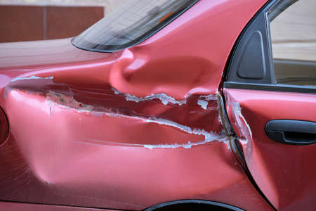 Dented car with damaged body parked on city street side. Road safety and vehicle insurance conceptの写真素材