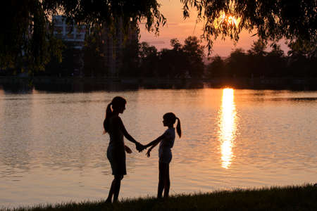 Happy mom and daughter girl relaxing holding hands enjoying time together in summer park at sunset. Family love and relationship conceptの写真素材