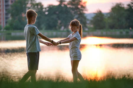 Happy siblings standing together holding hands in summer park. Young children brother and sister relaxing outdoors. Family love and relationship conceptの写真素材
