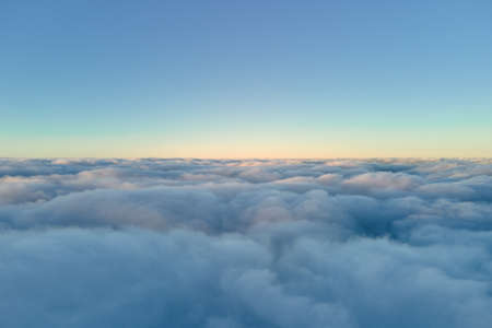 Aerial view from airplane window at high altitude of dense puffy cumulus clouds flying in eveningの写真素材