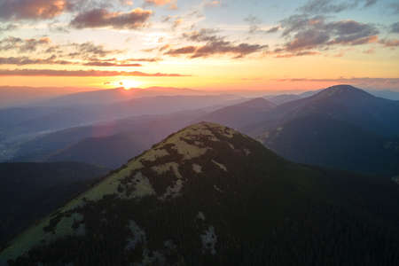 Aerial view of amazing scenery with foggy dark mountain peak covered with forest pine trees at autumn sunrise. Beautiful wild woodland with shining rays of light at dawnの写真素材