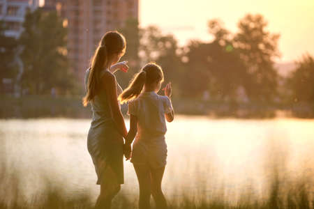 Happy mom and daughter girl standing together looking at apartment building under construction dreaming about their future home in evening. Family love and plans about future conceptの写真素材