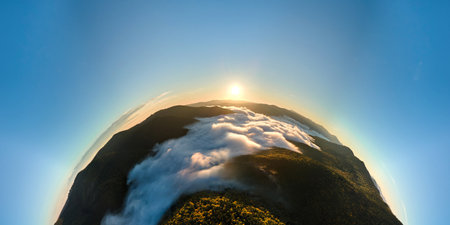 Aerial view from high altitude of little planet earth at sunrise covered with evergreen forest and high mountain peaksの写真素材
