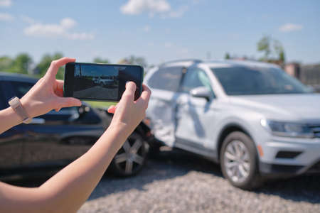 Stressed driver taking picture on sellphone camera of smashed ve