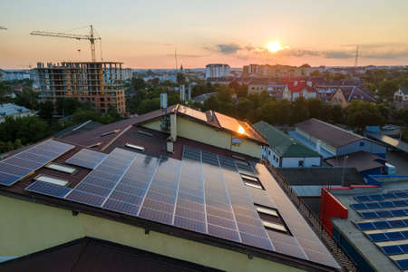 Blue photovoltaic solar panels mounted on building roof for producing clean ecological electricity at sunset. Production of renewable energy conceptの写真素材