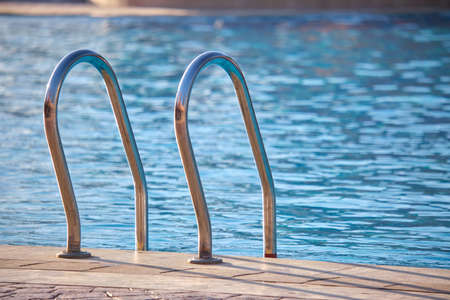 Close up of swimming pool stainless steel handrail descending into tortoise clear pool water. Accessibility of recreational activities conceptの写真素材