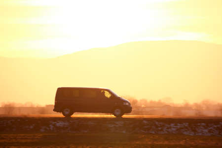 Passenger van driving fast on intercity road at sunset. Highway traffic in evening