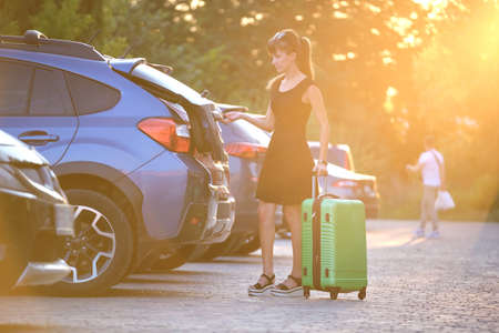 Young female driver putting luggage suitcase bag inside her car. Travelling and vacations conceptの写真素材