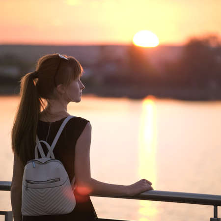 Young woman in casual outfit relaxing on lake side on warm evening. Summer vacations and travelling...