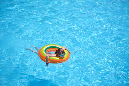 Portrait of happy child girl relaxing in inflatable circle in swimming pool on sunny summer day...
