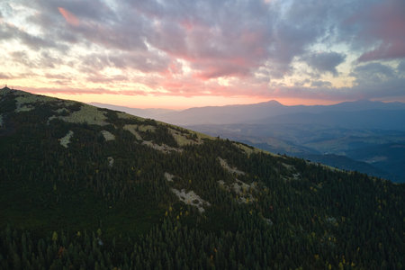 Aerial view of amazing scenery with foggy dark mountain peak covered with forest pine trees at autumn sunrise. Beautiful wild woodland with shining rays of light at dawn.の写真素材