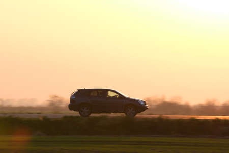 SUV car driving fast on intercity road at sunset. Highway traffic in evening