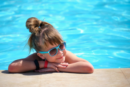 Young joyful child girl resting on swimming pool side with clear blue water on sunny summer day. Tropical vacations conceptの写真素材