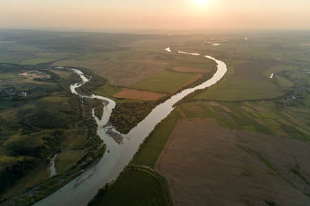 Aerial landscape view of village houses and distant green cultivated agricultural fields with growing crops on bright summer dayの写真素材