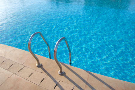 Close up of swimming pool stainless steel handrail descending into tortoise clear pool water....