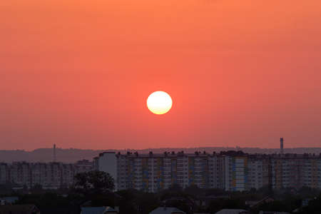 Evening landscape with bright setting sun over distant city high rise buildings at sunset