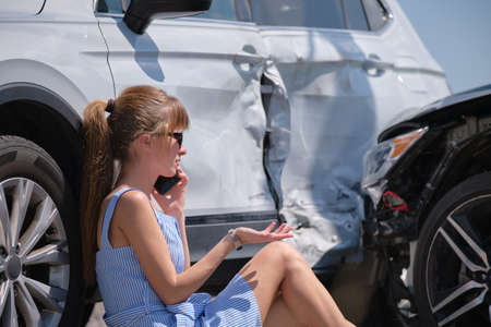 Sad female driver speaking on sellphone on street side calling for emergency service after car...