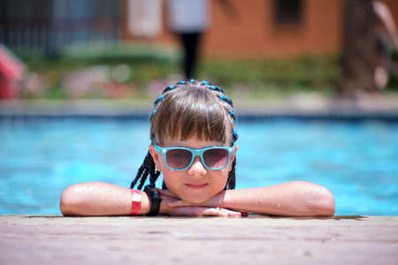 Young joyful child girl resting on swimming pool side with clear blue water on sunny summer day. Tropical vacations conceptの写真素材