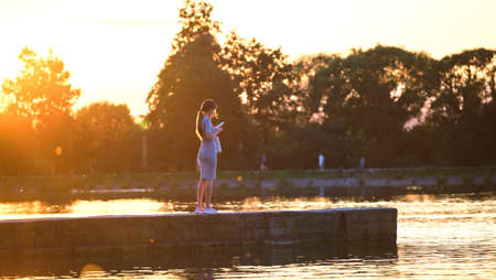 Rear view of lonely woman standing alone on lake shore on warm evening. Solitude and relaxing in nature conceptの写真素材