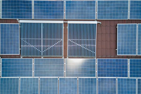 Building roof with rows of blue photovoltaic panels and vacuum air solar collectors for water...