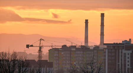 Dark silhouette of tower cranes at high residential apartment buildings construction site at sunset....