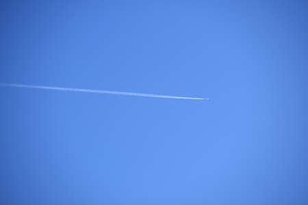Distant passenger jet plane flying on high altitude on clear blue sky leaving white smoke trace of...