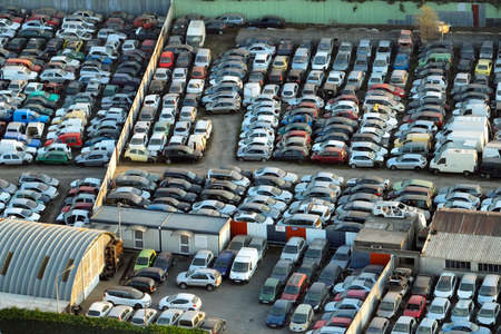 Aerial view of big parking lot of junkyard with rows of discarded broken cars. Recycling of old...