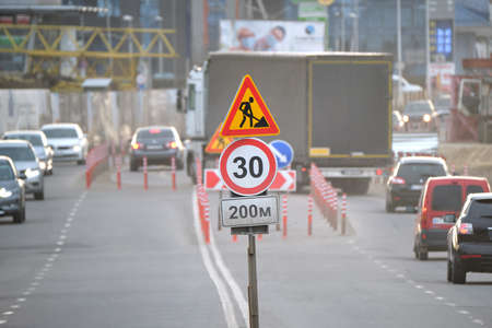 Roadworks warning traffic signs of construction work on city street and slowly moving cars