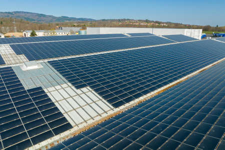 Aerial view of solar power plant with blue photovoltaic panels mounted on industrial building roof...