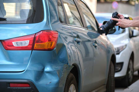Insurance worker taking photo on camera of dented fender on street side for emergency service after car accident. Road safety and insurance conceptの写真素材