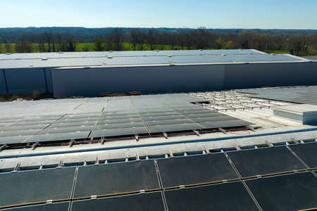 Aerial view of blue photovoltaic solar panels mounted on industrial building roof for producing...
