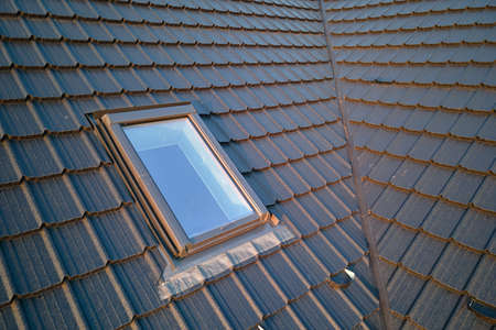 Closeup of attic window on house roof top covered with ceramic shingles. Tiled covering of buildingの写真素材
