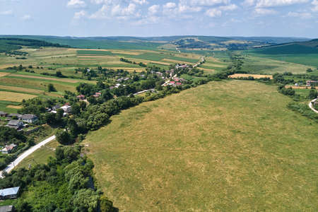Aerial landscape view of village houses and distant green cultivated agricultural fields with...