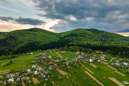 Aerial landscape view of village houses and distant green cultivated agricultural fields with growing crops on bright summer dayの写真素材