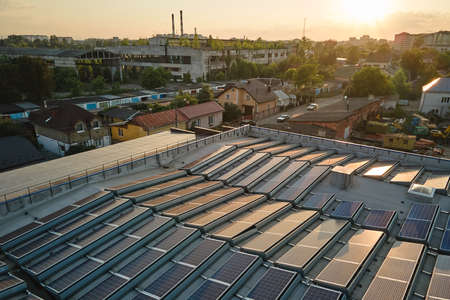 Aerial view of blue photovoltaic solar panels mounted on industrial building roof for producing green ecological electricity at sunset. Production of sustainable energy conceptの写真素材