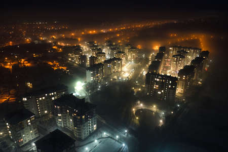 Aerial view of high rise apartment buildings and bright illuminated streets in city residential area at night. Dark urban landscapeの写真素材