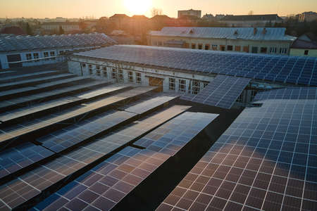 Aerial view of solar power plant with blue photovoltaic panels mounted on industrial building roof for producing green ecological electricity. Production of sustainable energy conceptの写真素材