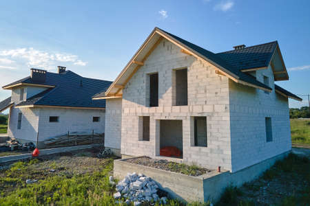 Aerial view of unfinished house with aerated lightweight concrete walls and wooden roof frame covered with metallic tiles under constructionの写真素材