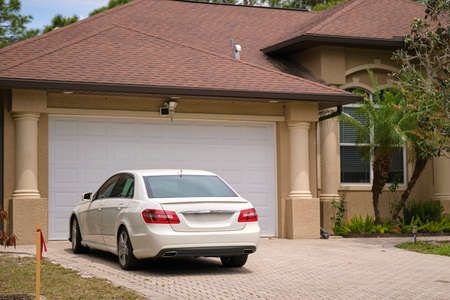 Vehicle parked in front of wide garage double door on paved driveway of typical contemporary american homeの写真素材