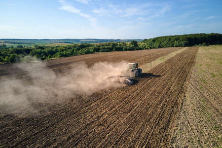 Aerial view of tractor plowing agriculural farm field preparing soil for seeding in summer