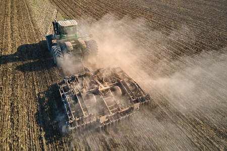 Aerial view of tractor plowing agriculural farm field preparing soil for seeding in summer