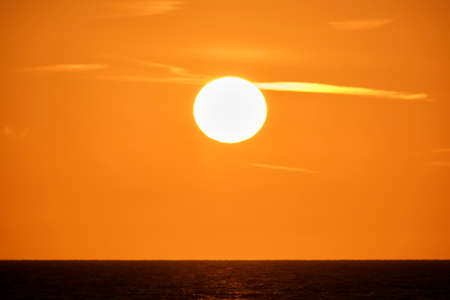 Ocean sunset. Big white sun on dramatic bright sky background, soft evening cloud over sea dark...
